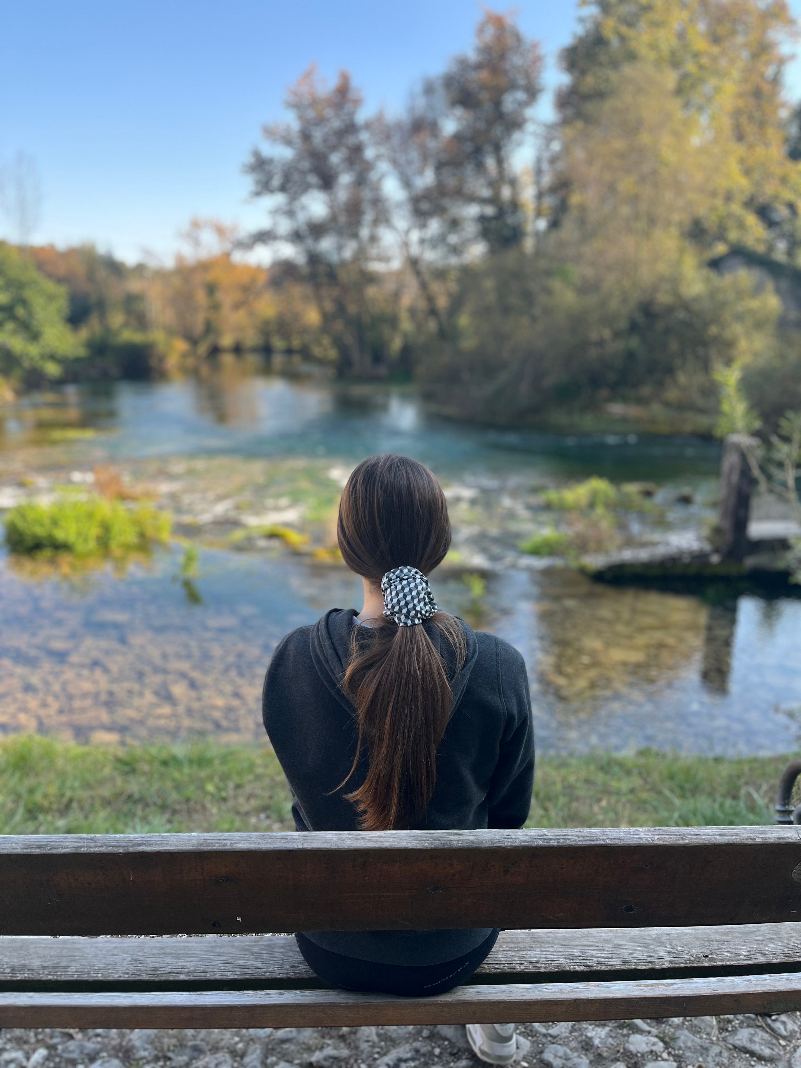 girl sitting on a bench watching a water spring and wearing a geometric headwear
